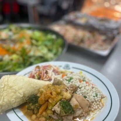A plated Chef Skills meal — chicken curry, couscous, salad and a wrap on a branded plate.