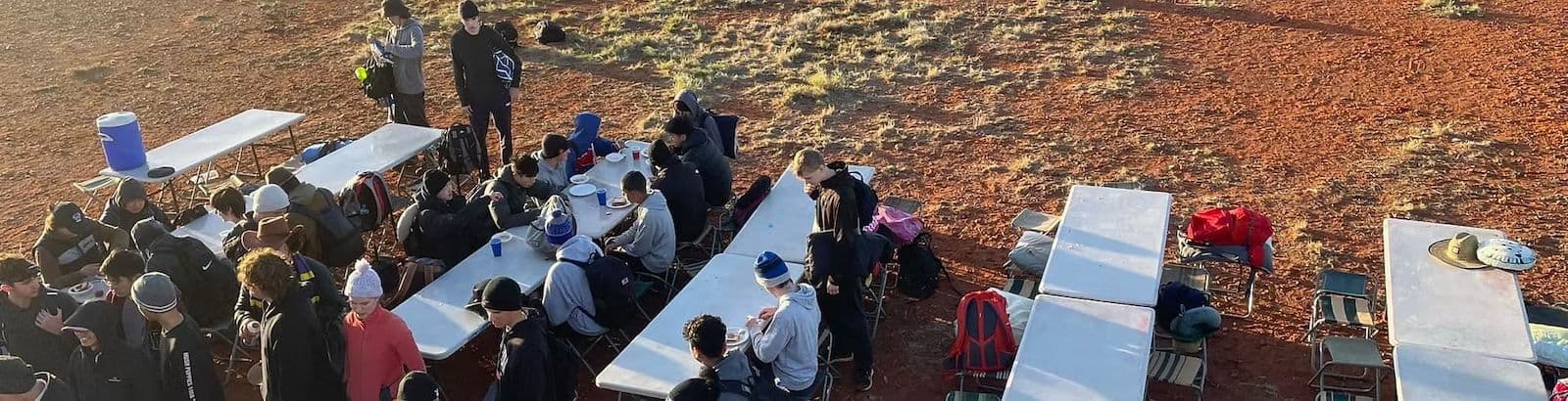 Students eating a meal at white trestle tables on red outback dirt during a Chef Skills school camp tour.